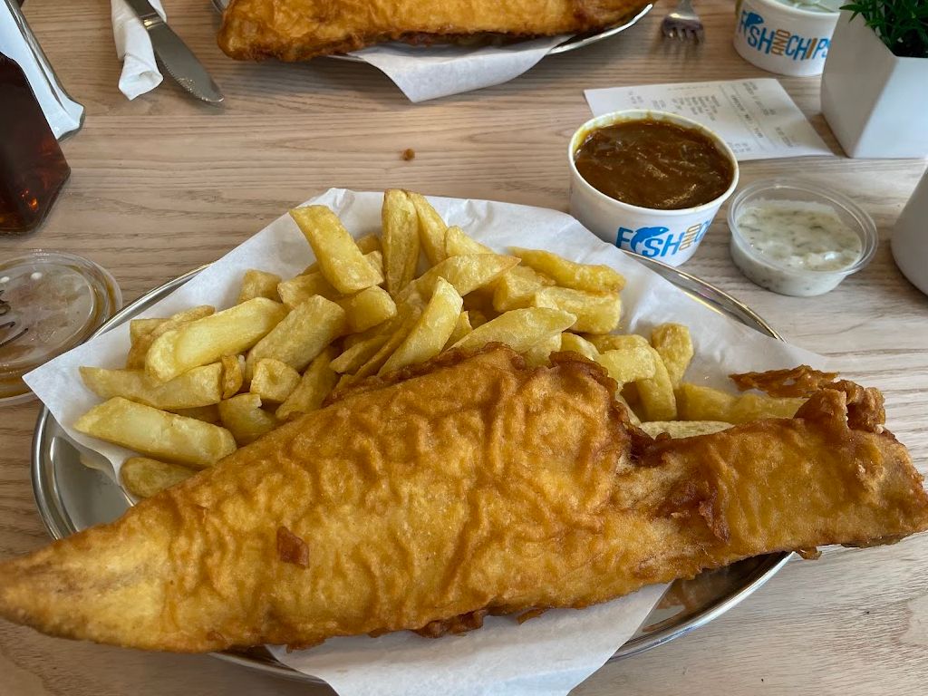 A plate full of fish and chips, curry sauce and tartare sauce